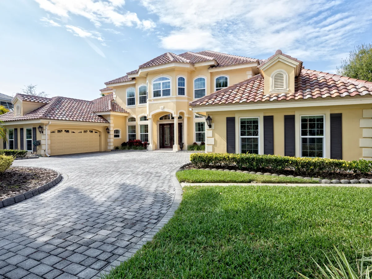 Grey paver driveway with a darker edge course sweeping up to a tile roofed home
